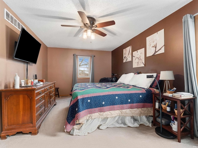 bedroom with light carpet, ceiling fan, visible vents, and a textured ceiling