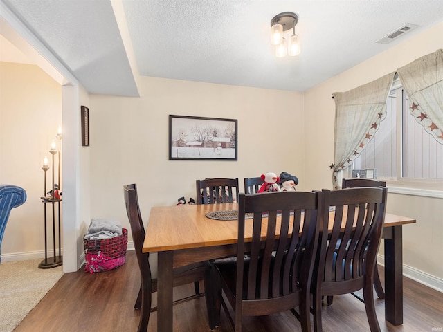 dining space with visible vents, a textured ceiling, baseboards, and wood finished floors