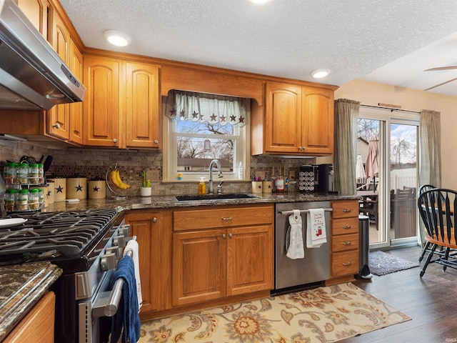 kitchen with stainless steel appliances, a sink, light wood-type flooring, range hood, and dark stone counters