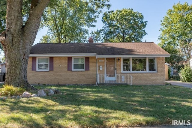 ranch-style house featuring a shingled roof, a chimney, a front lawn, and brick siding