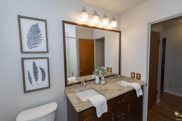 full bathroom with wood finished floors, a sink, toilet, and double vanity