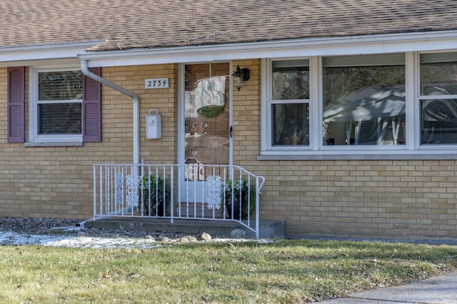 doorway to property featuring a shingled roof and brick siding