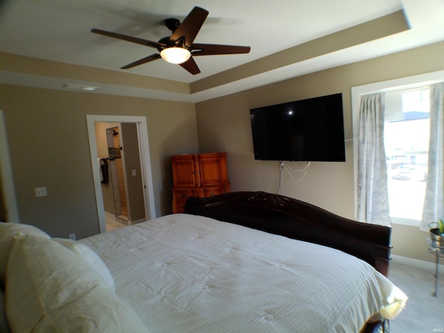 bedroom with a ceiling fan, a tray ceiling, multiple windows, and light carpet