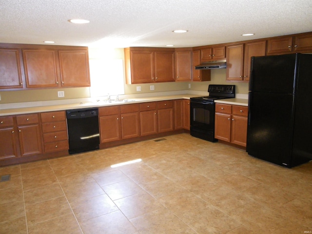 kitchen with brown cabinets, under cabinet range hood, light countertops, a textured ceiling, and black appliances