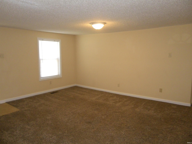 spare room with dark colored carpet, visible vents, a textured ceiling, and baseboards