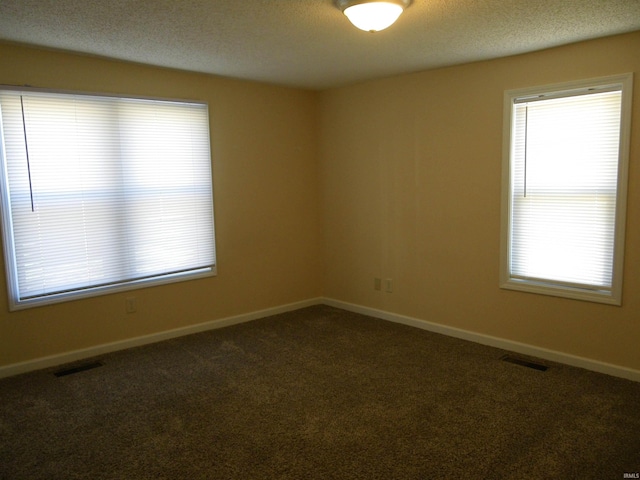 unfurnished room featuring a wealth of natural light, dark carpet, and visible vents