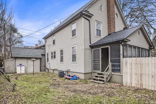 back of house featuring an outbuilding, metal roof, central air condition unit, a sunroom, and a chimney