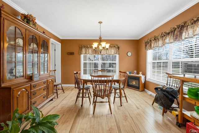 dining space featuring baseboards, a glass covered fireplace, light wood-style flooring, and an inviting chandelier