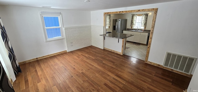 unfurnished room with a sink, a wainscoted wall, visible vents, and dark wood-type flooring