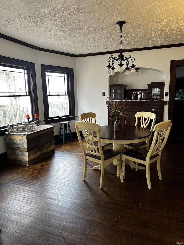 dining room with a textured ceiling, dark wood-style flooring, a notable chandelier, and crown molding