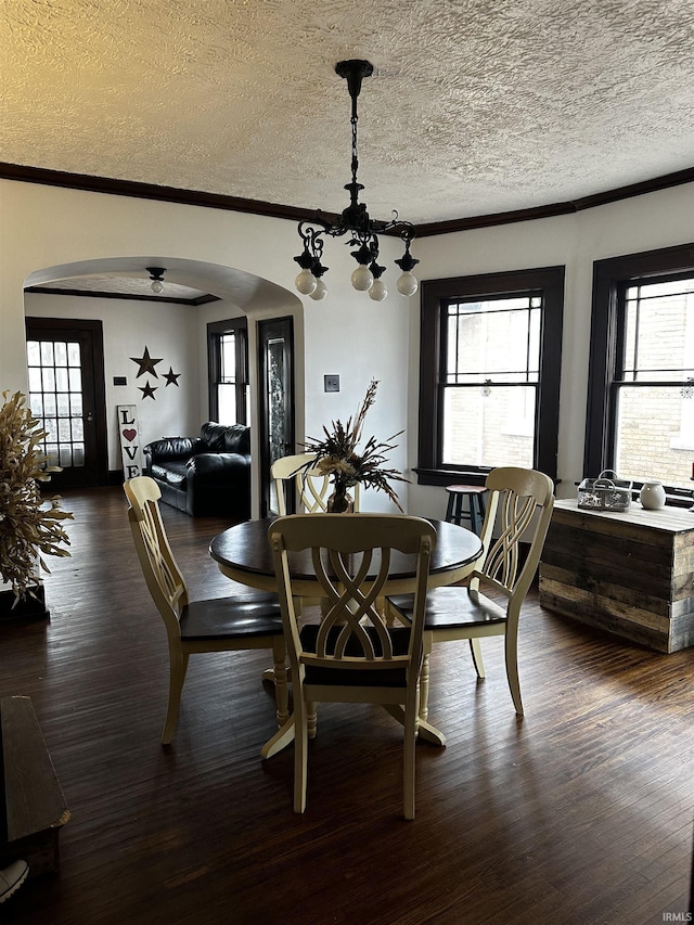 dining space with arched walkways, dark wood-type flooring, and ornamental molding