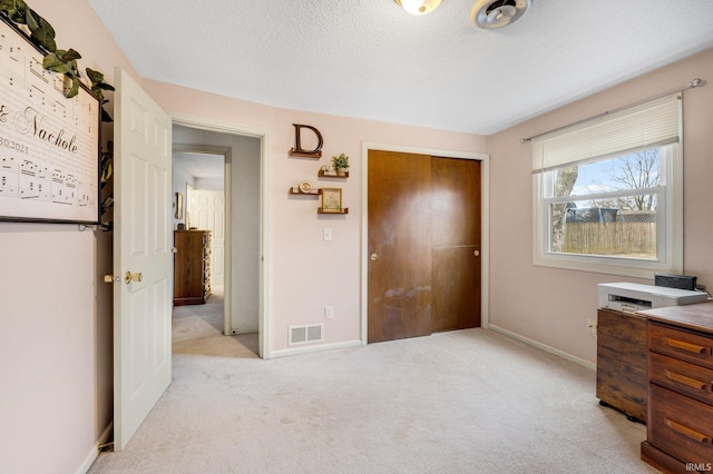 bedroom with a textured ceiling, light carpet, visible vents, baseboards, and a closet