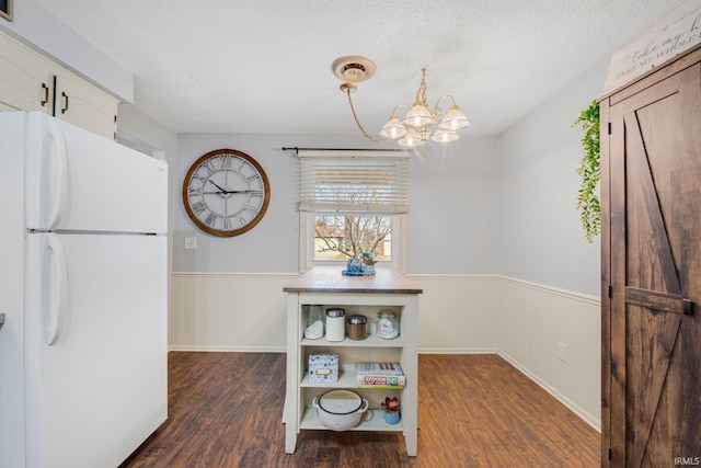 dining room with a textured ceiling, a chandelier, dark wood-type flooring, and wainscoting