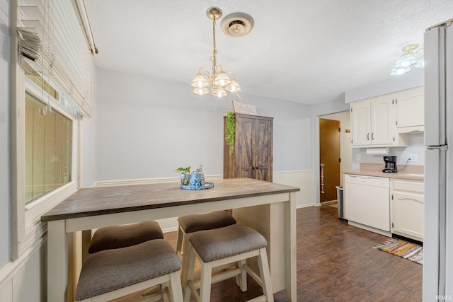 kitchen with dark wood-style floors, light countertops, hanging light fixtures, white cabinetry, and dishwasher