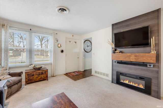 carpeted living area with visible vents, a textured ceiling, and a glass covered fireplace