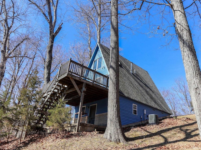 view of side of property with a deck, central AC unit, and roof with shingles