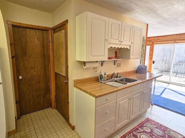 kitchen with a textured ceiling, a sink, white cabinets, light countertops, and light floors