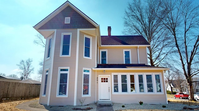 view of front facade featuring a shingled roof, fence, and a chimney