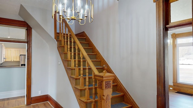 stairway featuring an inviting chandelier, plenty of natural light, baseboards, and wood finished floors