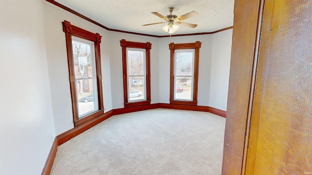 carpeted spare room featuring a ceiling fan, a textured ceiling, baseboards, and crown molding