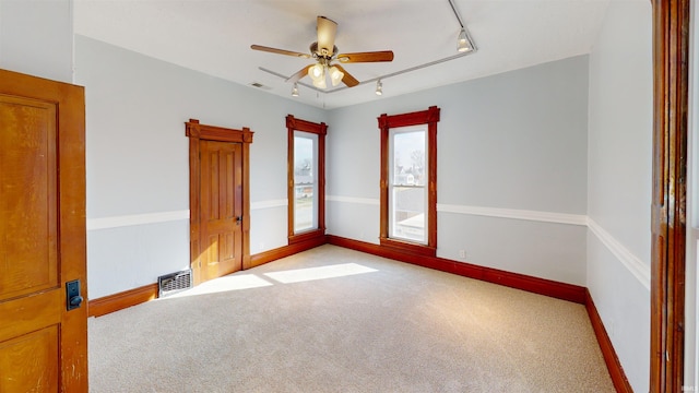 carpeted empty room with track lighting, visible vents, ceiling fan, and baseboards