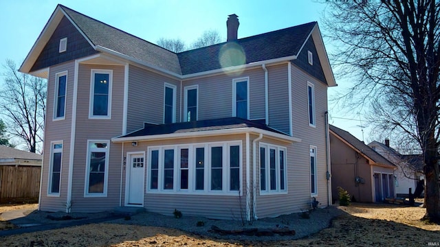 rear view of house with a shingled roof, a chimney, and fence