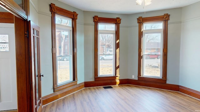 unfurnished room featuring a healthy amount of sunlight, visible vents, baseboards, and wood finished floors