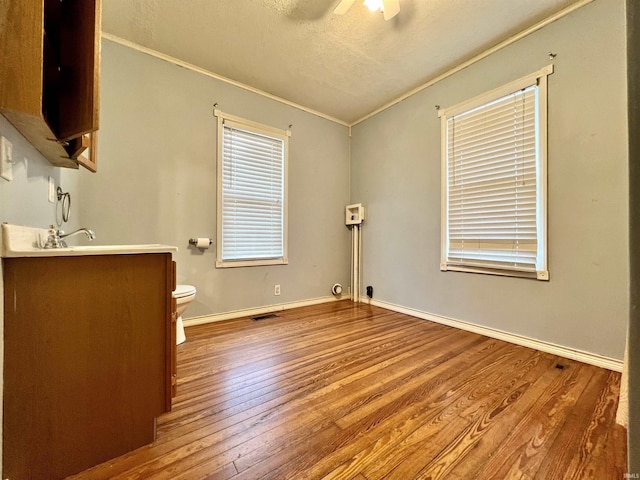 interior space with baseboards, visible vents, a ceiling fan, wood-type flooring, and crown molding