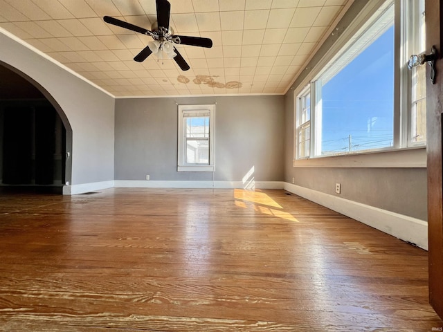 unfurnished living room with baseboards, arched walkways, crown molding, and wood finished floors