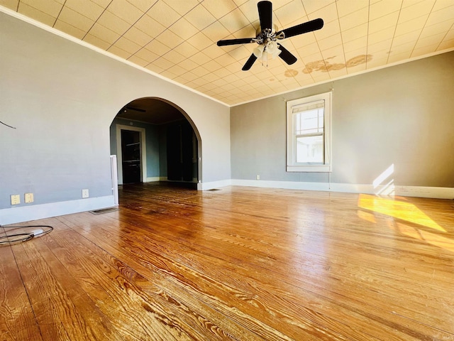 empty room featuring arched walkways, baseboards, wood finished floors, and crown molding