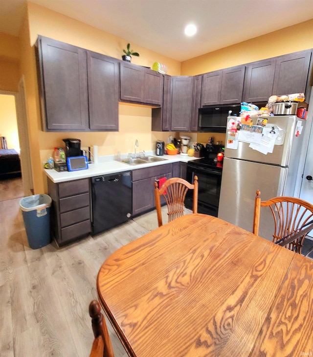 kitchen featuring light countertops, light wood-style flooring, dark brown cabinetry, a sink, and black appliances