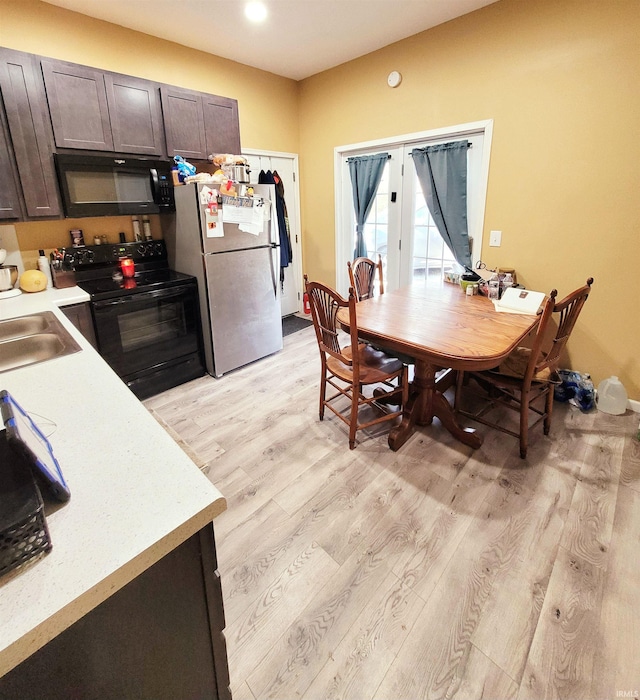 kitchen with light countertops, light wood-style flooring, a sink, dark brown cabinets, and black appliances