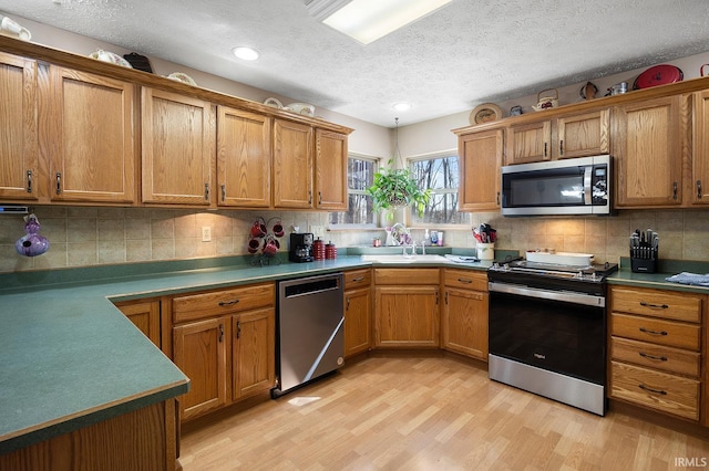 kitchen featuring stainless steel appliances, brown cabinetry, a sink, and light wood-style flooring