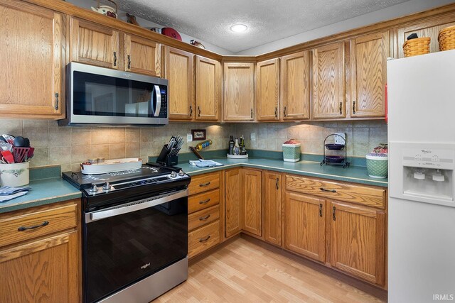 kitchen with brown cabinetry, light wood-style flooring, stainless steel appliances, and a textured ceiling