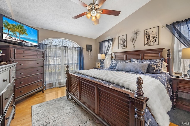 bedroom with light wood-style floors, ceiling fan, vaulted ceiling, and a textured ceiling