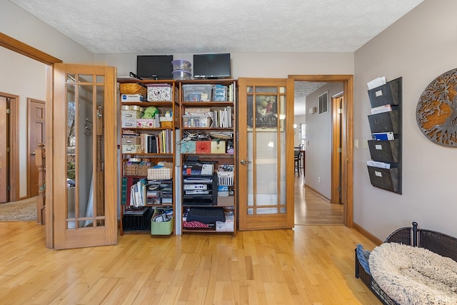 interior space with french doors, a textured ceiling, baseboards, and wood finished floors