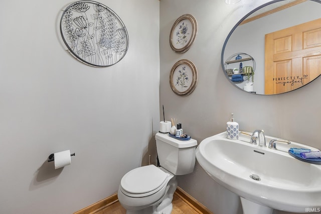 half bath with toilet, baseboards, and a sink