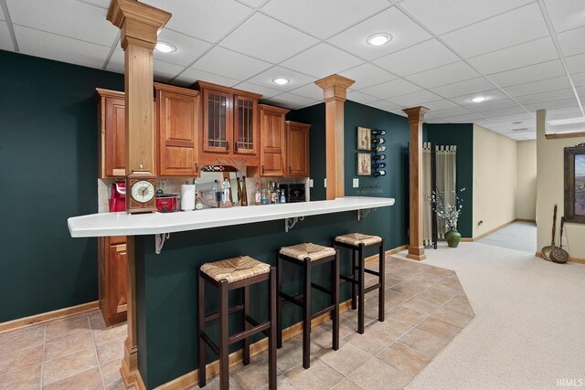 bar featuring light carpet, a drop ceiling, decorative columns, and baseboards