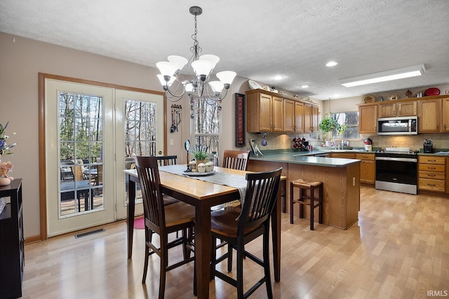 dining room featuring a textured ceiling, a chandelier, recessed lighting, visible vents, and light wood-type flooring