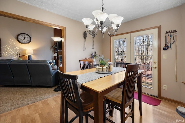 dining space with light wood finished floors, baseboards, a textured ceiling, and an inviting chandelier