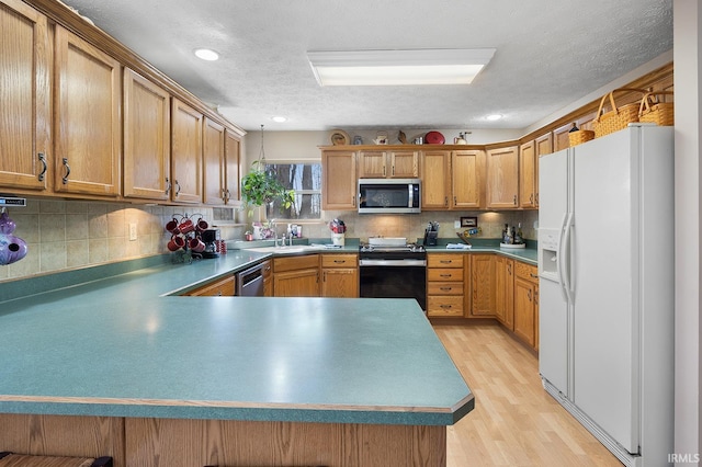 kitchen with light wood finished floors, backsplash, a peninsula, stainless steel appliances, and a sink