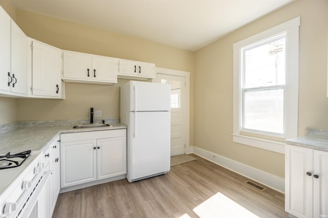 kitchen featuring visible vents, light wood-type flooring, a sink, white appliances, and baseboards