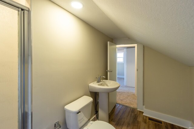 bathroom with visible vents, toilet, a textured ceiling, wood finished floors, and lofted ceiling