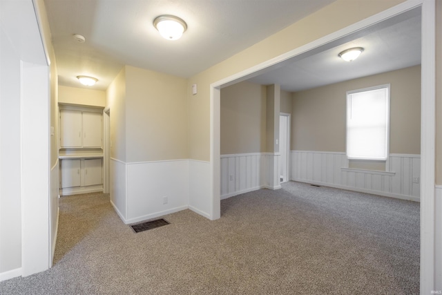 unfurnished room featuring carpet flooring, visible vents, and wainscoting