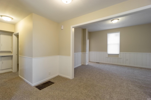 empty room with visible vents, light carpet, and a wainscoted wall