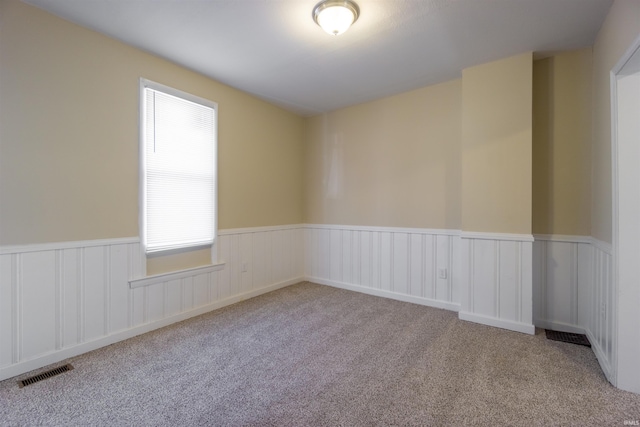 carpeted spare room featuring visible vents and a wainscoted wall