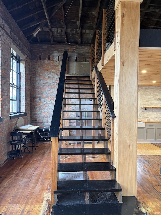 staircase featuring wood-type flooring, lofted ceiling, and brick wall