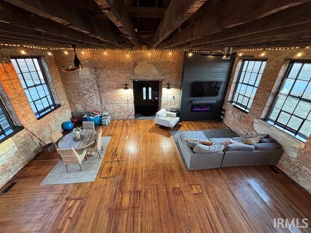 unfurnished living room featuring beamed ceiling, brick wall, a fireplace, and hardwood / wood-style flooring