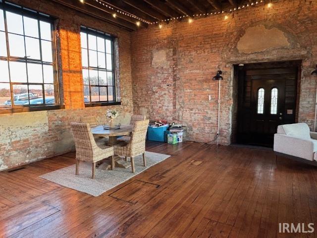 unfurnished dining area featuring track lighting, a high ceiling, brick wall, and wood-type flooring