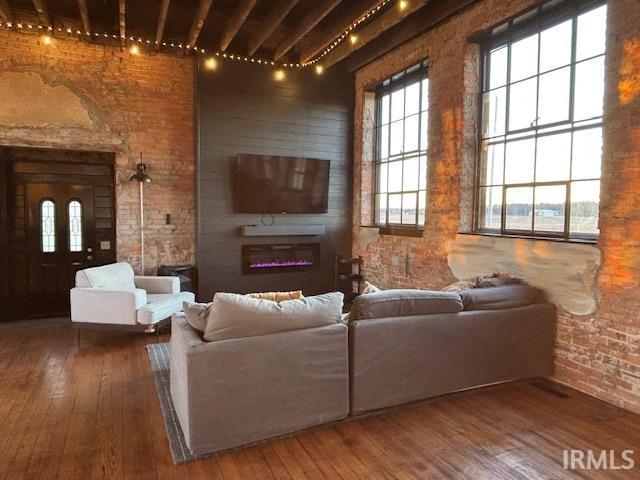 living room featuring hardwood / wood-style floors, a glass covered fireplace, a healthy amount of sunlight, and brick wall